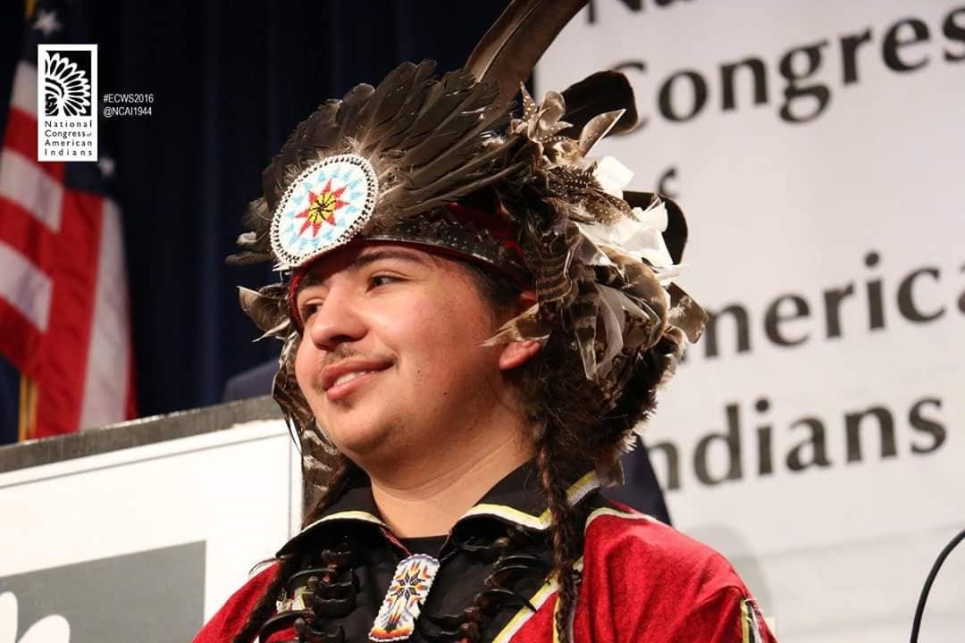 A young Indigenous man wearing a headdress and smiling