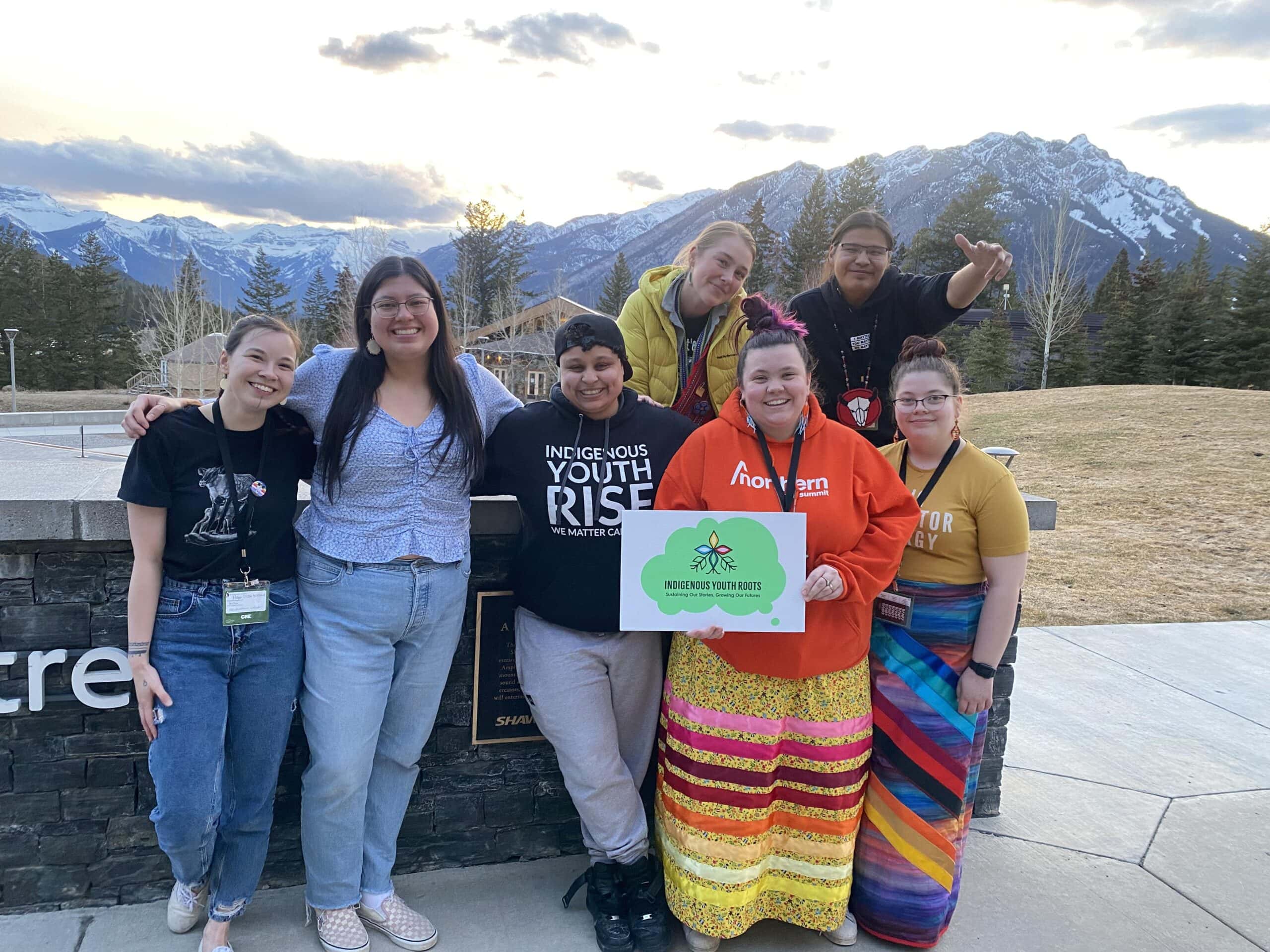 A group of Indigenous youth post for a photo in front of mountains in Banff.