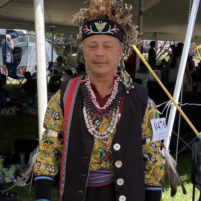 An older person wearing regalia at a powwow