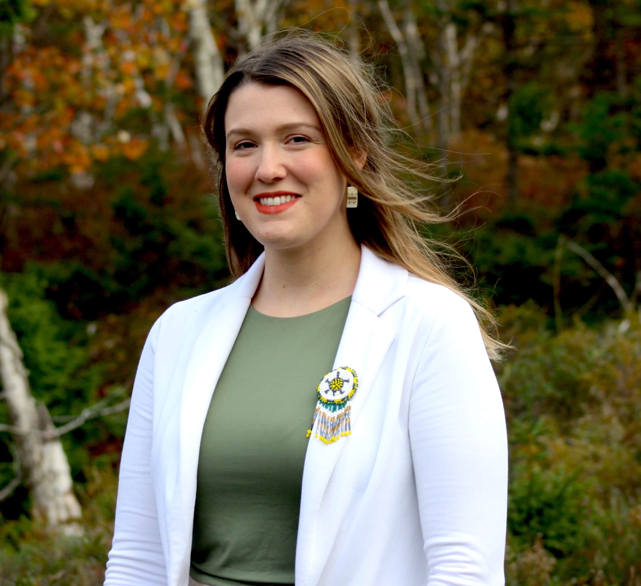 Chelsey Purdy, who has long light brown hair smiles for a photo while wearing a white blazer and green shirt underneath