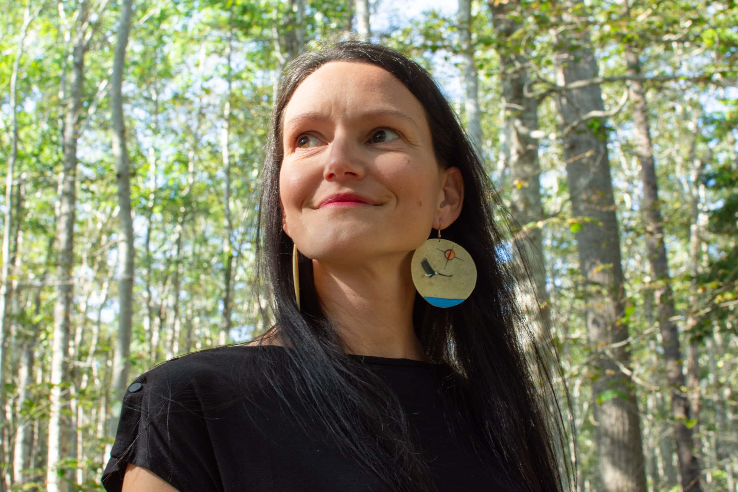 Lisa Neault has long black hair, wears beaded earrings and stands in a forest